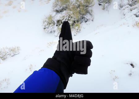 Eine links, schwarz behandschuhten Hand zeigen einen Daumen nach oben in den Schnee. Stockfoto