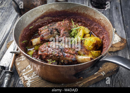 Lamm Knuckles mit Bratkartoffeln in Burgund Soße in Kasserolle Stockfoto