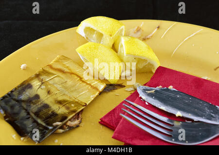 Reste von geräuchertem Fisch, Zitronen und schmutziges Geschirr Stockfoto