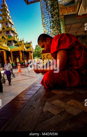 Mönch auf sein Handy in der Shwedagon Pagode in Yangon, Myanmar Stockfoto