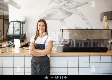 Kaffee Business Owner Konzept - Portrait von Happy attraktiven jungen schönen kaukasischen Barista in Schürze Kamera im Coffee shop Zähler lächelnd. Stockfoto