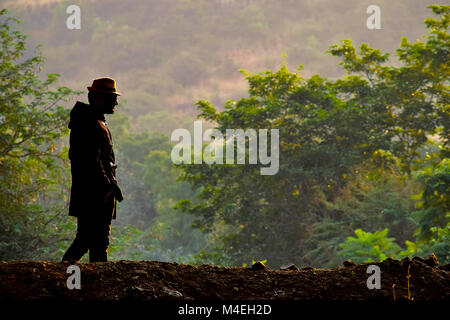 Mann in einem Hut und schwarzen Jacke vor einem grünen Hintergrund, Pune, Maharashtra hervorgehoben. Stockfoto