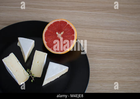 Brie Käse und Grapefruit auf einer schwarzen Platte whit Freier Speicherplatz Stockfoto
