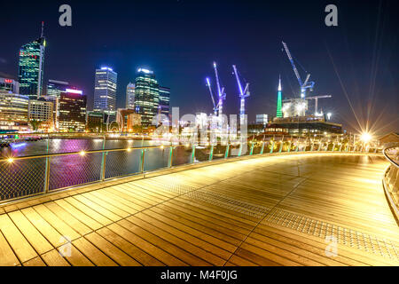 Perth, Australien - Jan 5, 2018: holzsteg von Elizabeth Quay Fußgängerbrücke durch die Nacht in Elizabeth Quay Marina beleuchtet. Central Business District und Baukräne auf Hintergrund. Stockfoto