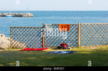 Hölzerne Balustrade am Meer, mit Kleidung und einen Rucksack, ein paar Schuhe und ein Paar Badetücher auf dem Gras lehnte Stockfoto
