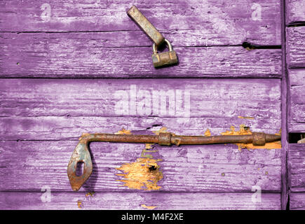 Close-up auf einem alten lila Holztür mit abblätternder Farbe und rostige Verriegelung und Griff Stockfoto
