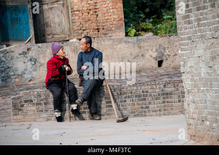 Ein alter Bauer an eine Wand im Gespräch mit einer älteren Dame in der Ming-dynastie Dorf Dangjiacun in der Nähe von Hancheng, Provinz Shaanxi, China sitzen. Stockfoto