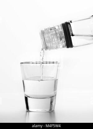 Wodka wird in ein Glas gegossen. Weißer Hintergrund. Stockfoto