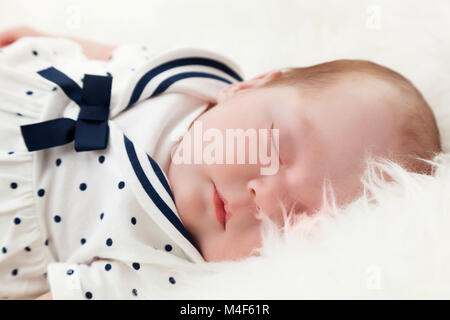 Neugeborene schlafen auf weißem Fell Decke. Das Tragen von Sailor Kleid. Stockfoto