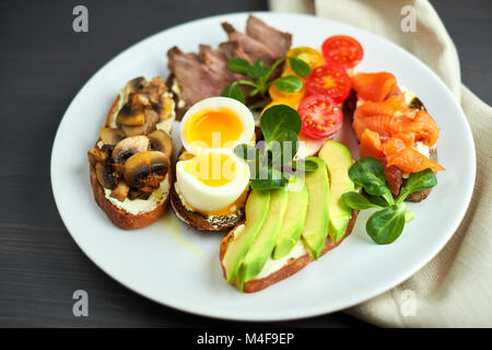 Bruschetta, sortiert, verschiedene Füllungen, auf Platten mit einem weich gekochten Ei in der Mitte Stockfoto