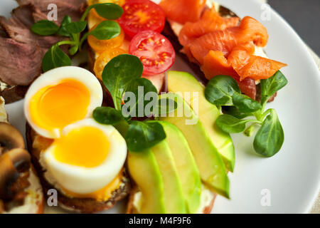 Bruschetta, sortiert, verschiedene Füllungen, auf Platten mit einem weich gekochten Ei in der Mitte Stockfoto