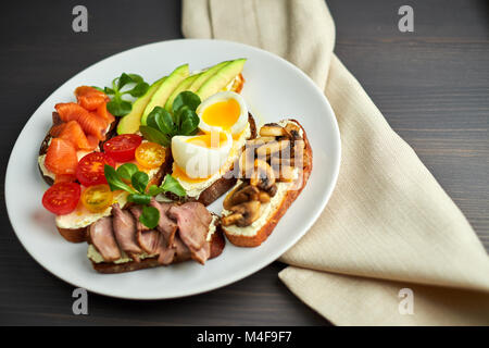 Bruschetta, sortiert, verschiedene Füllungen, auf Platten mit einem weich gekochten Ei in der Mitte Stockfoto