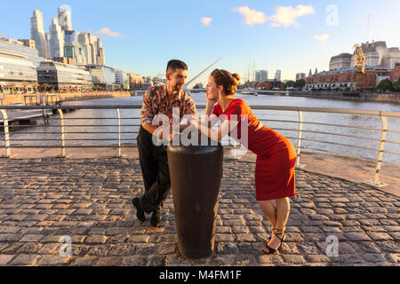 Ein junges Paar in Puerto Madero bei Sonnenuntergang, mit der "Puente de la Mujer" im Hintergrund. Buenos Aires, Argentinien. Stockfoto