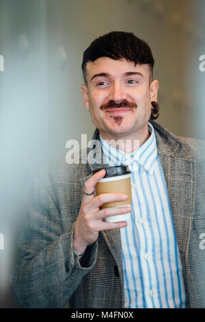 Unternehmer aus seinem Büro Fenster mit einer Tasse Kaffee in der Hand. Stockfoto