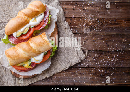 Foto von Sandwich mit Gemüse und Wurst auf Papier auf Tisch Stockfoto