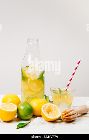 Natürliche Limonade mit Zitrone, Limette und Minze in einer Flasche mit Holz- Reibahle und Lemon Tree Blätter auf einem weißen Tisch Stockfoto