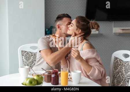 Porträt eines glücklich verliebten, das Frühstück am Tisch in einer Küche zu Hause sitzen und küssen Stockfoto