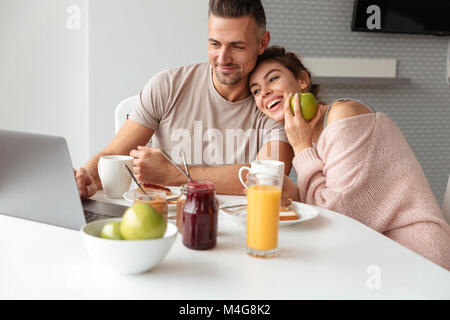 Lächelnd liebenden Paar beim Frühstück saßen am Tisch und mit Laptop Computer auf Küche Stockfoto