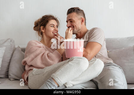 Glücklich liebend Paar sitzt auf der Couch zusammen und essen Popcorn zu Hause Stockfoto