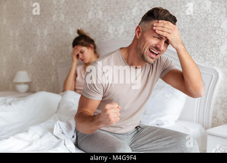 Sorgen Mann sitzt auf dem Bett mit seiner Freundin auf den Hintergrund zu Hause verwirrt Stockfoto