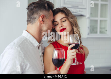 Junge hübsche Frau im roten Kleid, Wein trinken und genießen Küsse von ihrem stattlichen Mann Stockfoto