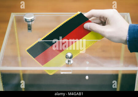 Mann einfügen Flagge von Deutschland in die Wahlurne, Abstimmungen und Wahlen in Deutschland. Stockfoto