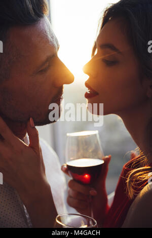 Junge wunderschöne Frau mit einem Glas Wein küsste ihren Mann im Sonnenuntergang Stockfoto