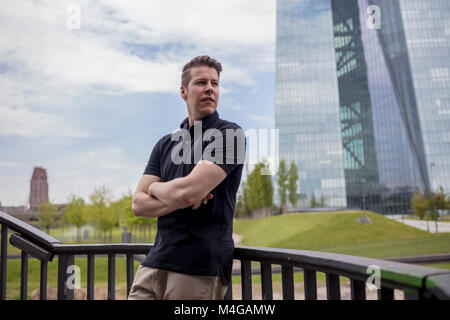 Ein Mann stand mit verschränkten Armen lehnte sich auf einer Balustrade und einem Hochhaus Gebäude im Hintergrund. Stockfoto