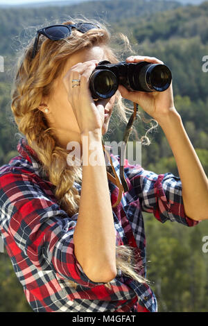 Junge blonde Frau, Tourist, auf einer Klippe mit einem Fernglas auf den Herbst Landschaft suchen. Russland, Sibirien, Salair Stockfoto