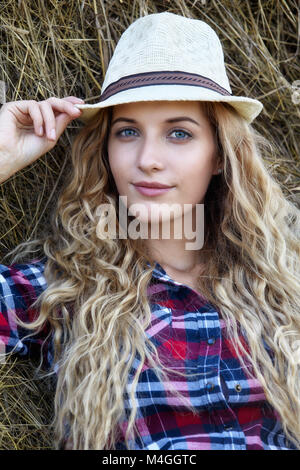 Jungen blonden Blauäugigen Land Frau in Hut sitzen in der Nähe von Heuballen Stockfoto