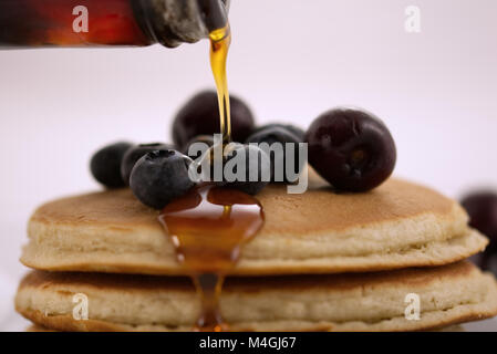 Frühstück Pfannkuchen mit Blaubeeren, Kirschen und Ahornsirup auf weißem Hintergrund mit sehr geringer Tiefenschärfe isoliert. Close up Frühstück Stockfoto