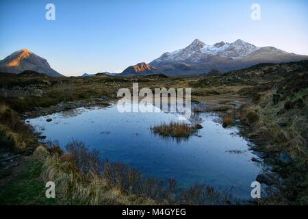 Blauer Himmel in einem kleinen Teich zu den schneebedeckten Gipfeln der Insel Skye, Schottland wider Stockfoto