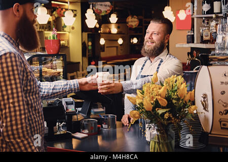 Positive bärtigen Barista männlich/Verkauf an einen Verbraucher in einem Coffee Shop. Stockfoto