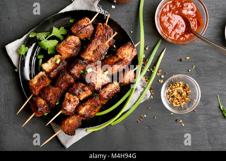 Gegrilltes Fleisch. Schwein am Spieß auf die Platte über der schwarzen Stein Hintergrund. Ansicht von oben, flach Stockfoto