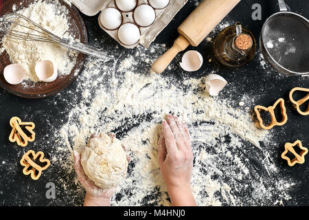 Die Frau Hände kneten Teig auf Tisch mit Mehl, Eiern und Zutaten auf Schwarz. Ansicht von oben. Immer noch leben. Flach Stockfoto