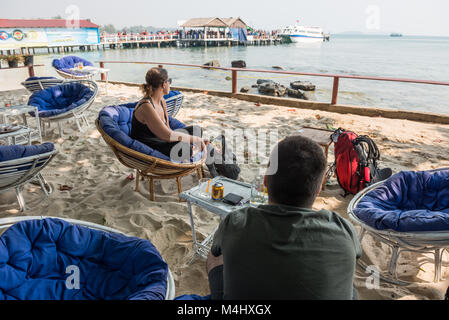 Zwei Touristen in den Sesseln in einer der Strandbars sitzen am Strand von Sihanoukville, Kambodscha die Ankunft einer Yacht erwarten. Stockfoto