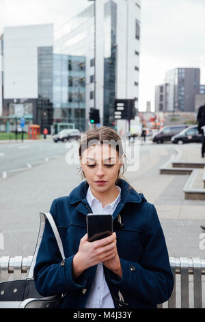 Junge Frau steht in der Stadt zu einem smart phone in ihre Hände. Stockfoto