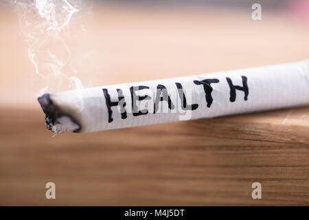 Nahaufnahme einer Gesundheit Wort auf brennende Zigarette auf hölzernen Schreibtisch geschrieben Stockfoto