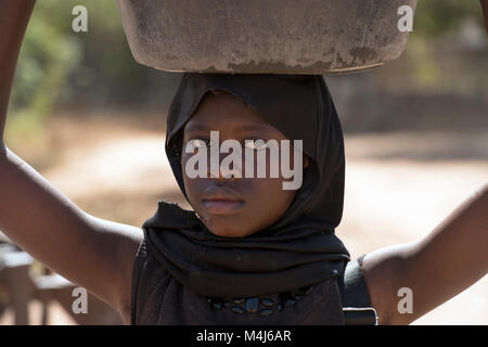 Eine junge mandinka (Mandingo) Mädchen mit einem Topf auf dem Kopf in ihrem Dorf in Gambia, Westafrika. Stockfoto