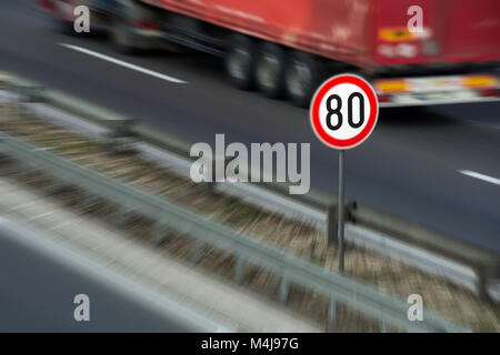 Defokussierten Bild von Verkehrszeichen mit 80 km/h Höchstgeschwindigkeit auf einer Autobahn mit roten Lkw im Hintergrund fahren Stockfoto