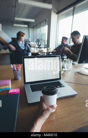 Geschäftsmann mit Kaffee, während die Kollegen in der Diskussion Stockfoto