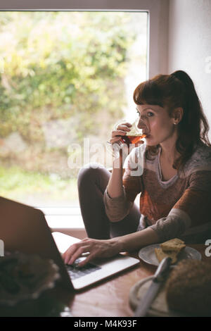 Frau mit Laptop, während mit Tasse Tee Stockfoto