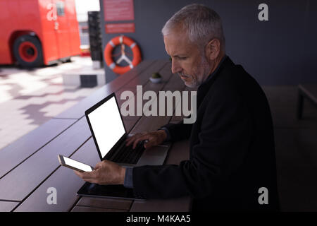 Mit Handy während der Arbeit am Laptop Geschäftsmann Stockfoto