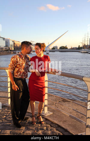 Ein junges Paar in Puerto Madero bei Sonnenuntergang, mit der "Puente de la Mujer" im Hintergrund. Buenos Aires, Argentinien. Stockfoto