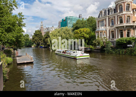 Blick auf einer von Bäumen gesäumten Kanal, Hop-on-Hop-off Tour Boot voller Touristen. Dieser Spot ist gegenüber dem beliebten Rijksmuseum entfernt. Stockfoto