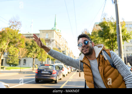 Stattliche Hipster mit orange Jacke und Sonnenbrille stoppen Taxi in der Stadt. Stockfoto