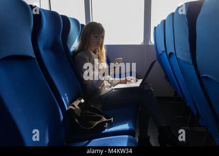 Frau Kontrolle Handy mit Laptop Stockfoto