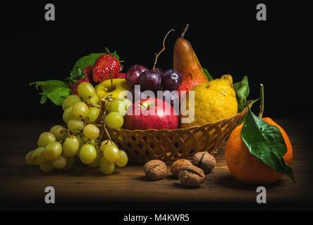 Weidenkorb mit herbstlichen Früchten auf schwarzem Hintergrund. Stockfoto