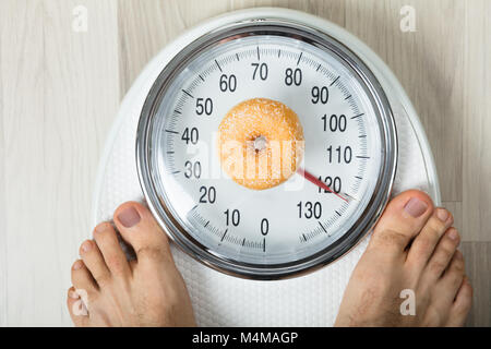 Nahaufnahme einer Person messen Gewicht mit Donut auf der Waage Stockfoto