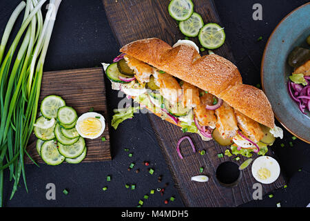 Baguette Sandwich mit Fisch, Ei, eingelegte Zwiebeln und Salatblätter. Ansicht von oben Stockfoto